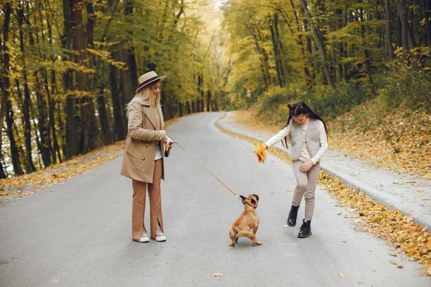 Mujer, niña y perro caminando en el parque de otoño