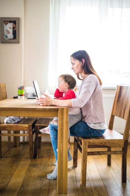 Mujer con niña en su regazo usando la computadora portátil