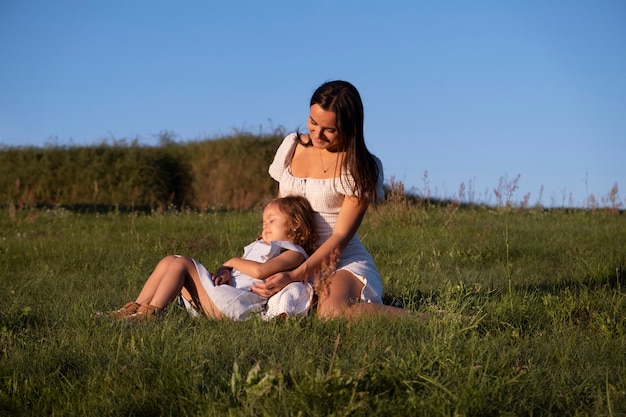 Foto gratuita mujer y niña de tiro completo sentadas al aire libre