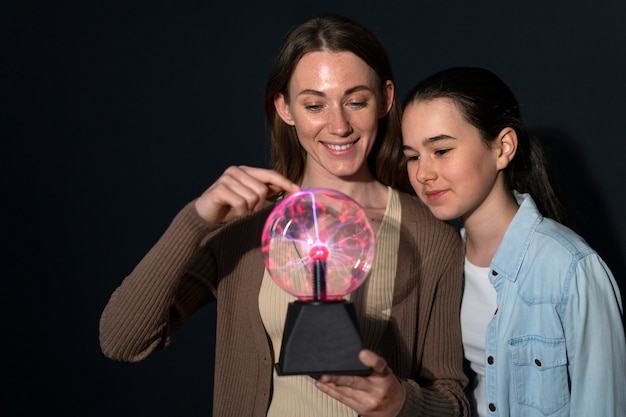 Mujer y niña de tiro medio interactuando con una bola de plasma