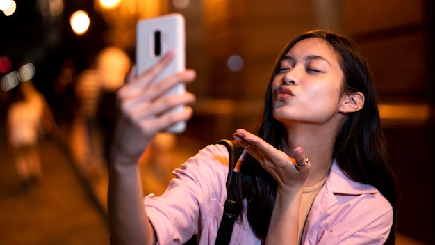 Mujer por la noche en las luces de la ciudad tomando selfie y enviando beso