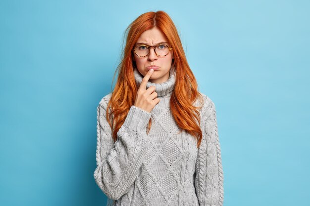 mujer ofendida molesta mantiene el dedo índice en los labios se ve infelizmente vestida con suéter de punto gris.