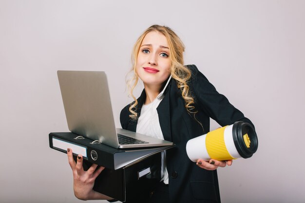 Mujer de oficina joven rubia linda en camisa blanca, chaqueta negra, con laptop, carpeta, café para llevar aislado. Expresando verdaderas emociones, éxito, trabajo, diversión