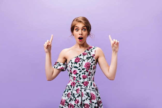 Una mujer de ojos abiertos con un vestido floral tiene una idea genial Una joven maravillosa y genial con ropa colorida a la moda posando sobre un fondo morado