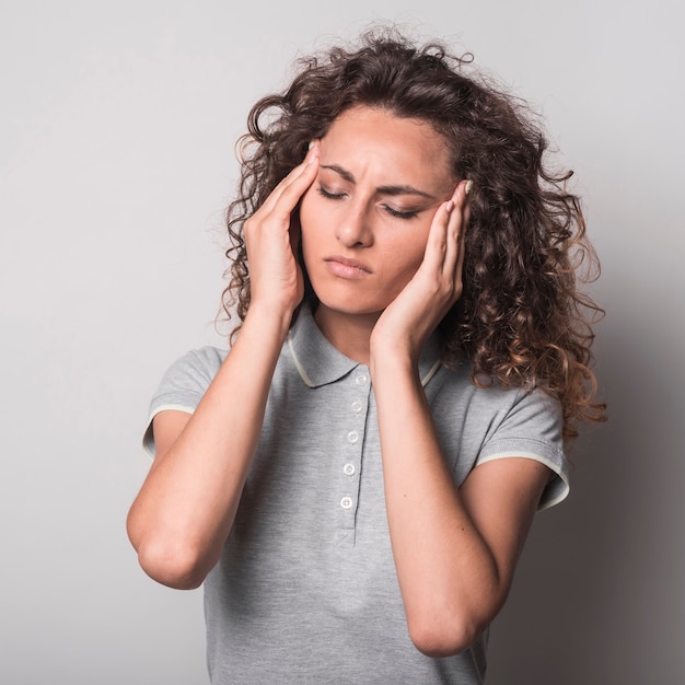 Mujer con los ojos cerrados con dolor de cabeza contra el fondo gris