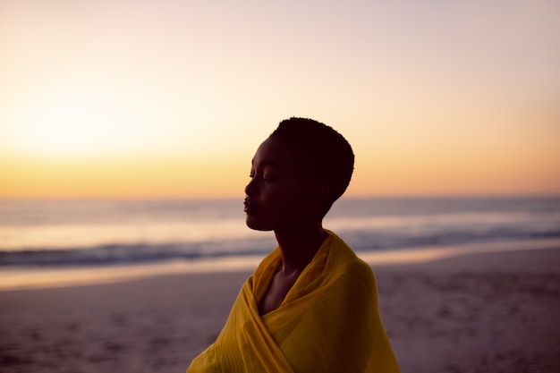 Mujer con los ojos cerrados envuelta en un pañuelo amarillo en la playa