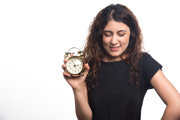 Mujer con ojos cerrados sosteniendo el reloj sobre fondo blanco. Foto de alta calidad