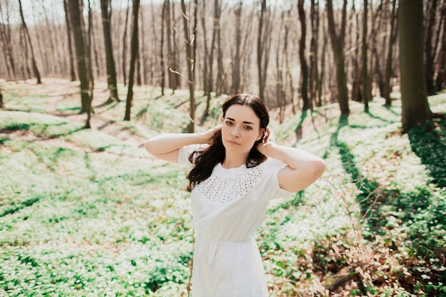 Mujer con ojos profundos poses en vestido blanco en el bosque