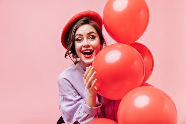 Mujer de ojos verdes con lápiz labial rojo se ríe y posa con globos sobre fondo aislado.