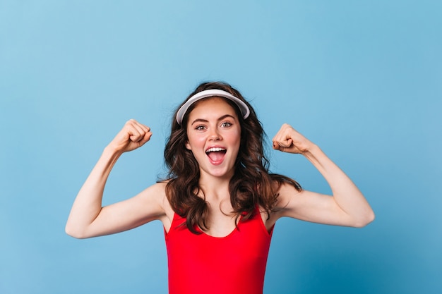 Mujer de ojos verdes positiva con gorra demuestra la fuerza de sus manos