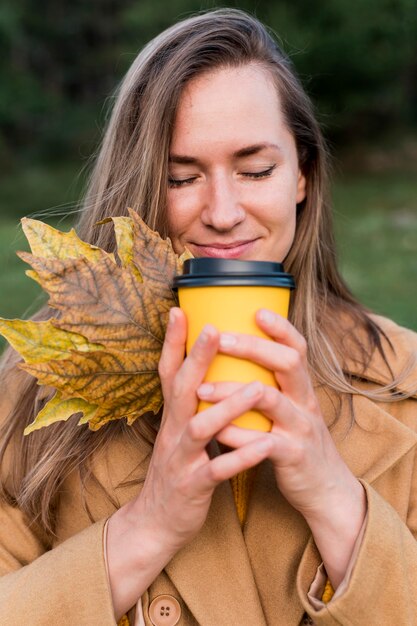 Mujer oliendo su café mientras sostiene algunas hojas