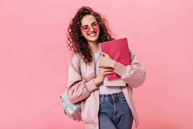 Mujer optimista en chaqueta de seda y jeans con cuadernos