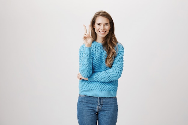 La mujer optimista sonriente muestra el signo de la paz