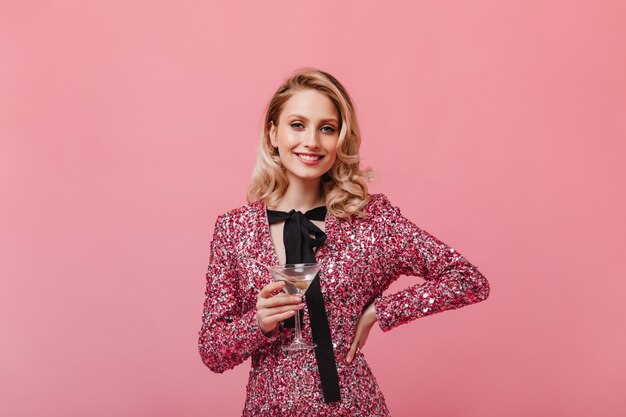 Mujer optimista en vestido elegante con sonrisa mira al frente y sostiene copa de martini