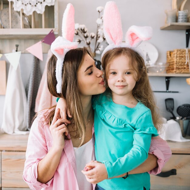 Mujer en orejas de conejo besando a hija en mejilla