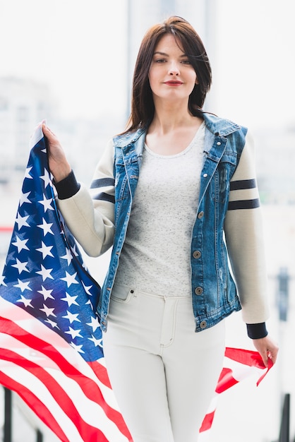 Mujer orgullosa caminando con gran bandera de Estados Unidos