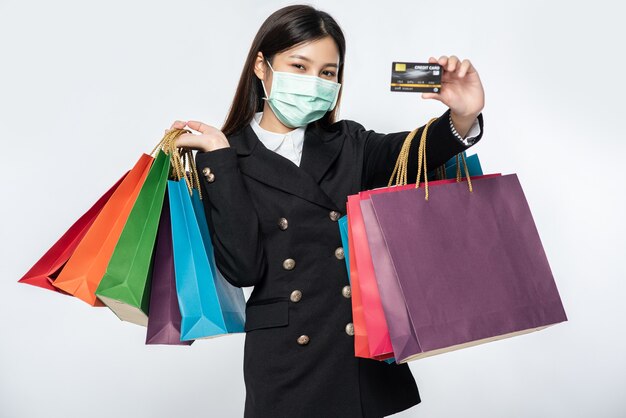 Una mujer en la oscuridad y con una máscara camina de compras, lleva tarjetas de crédito y muchas bolsas.