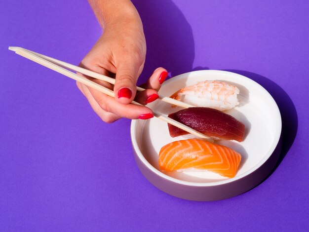 Mujer con palillos tomando un sushi de un tazón blanco