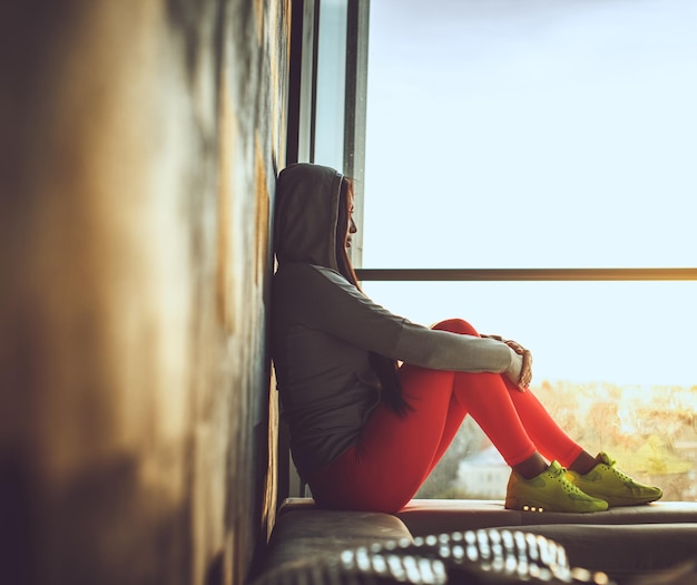 Mujer con pantalones rojos y zapatos amarillos sentada cerca de la ventana.