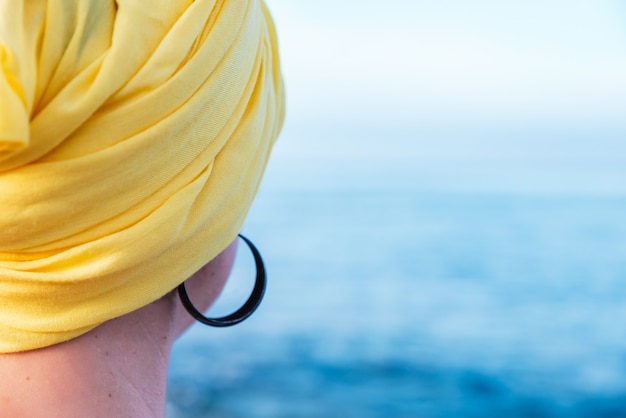 Mujer con un pañuelo amarillo disfrutando de la vista al mar - concepto: lucha contra el cáncer
