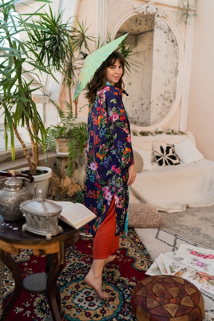 Mujer con paraguas japonés apareciendo en interior boho con plantas tropicales y muebles elegantes.