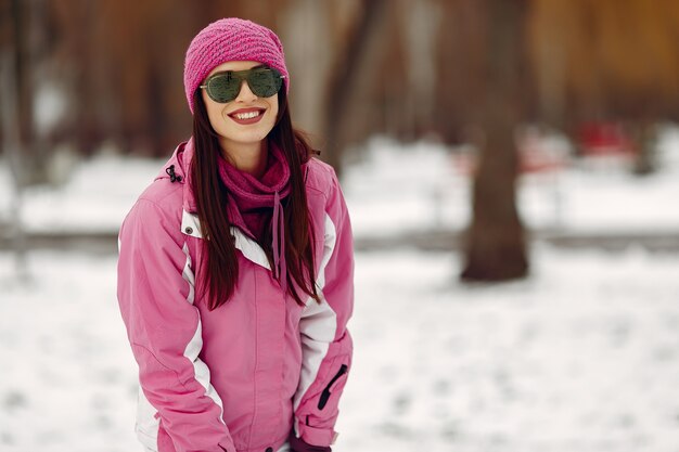 Mujer en un parque de invierno. Dama en traje deportivo rosa. Chica con gafas de sol.