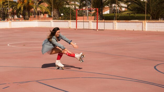 Mujer patinadora agachada y en equilibrio sobre una pierna en la cancha