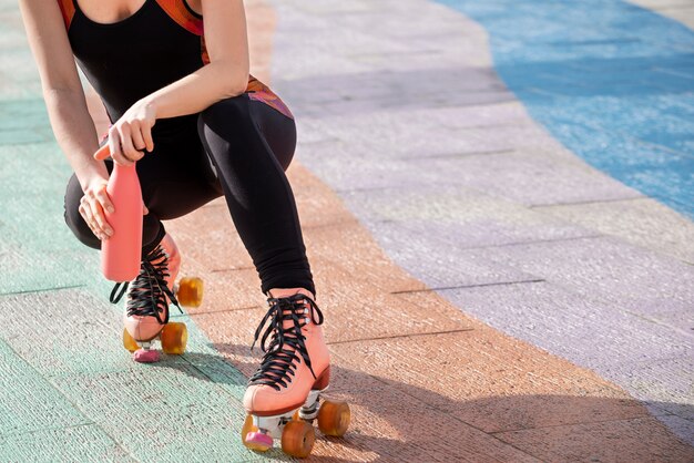 Mujer con patines abriendo una botella de agua al aire libre