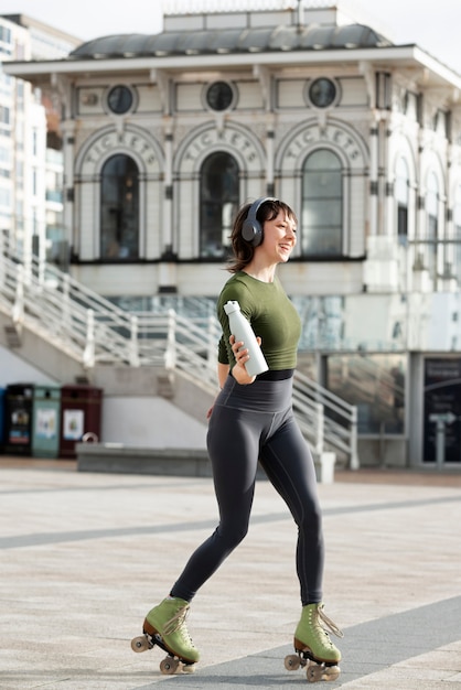 Mujer con patines bailando y sosteniendo una botella de agua al aire libre