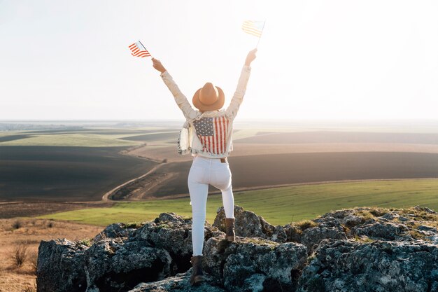 Mujer patriótica posando con banderas americanas en la cima de la montaña