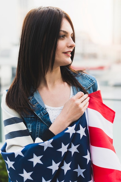 Mujer patriótica sonriente envuelta en la bandera de Estados Unidos