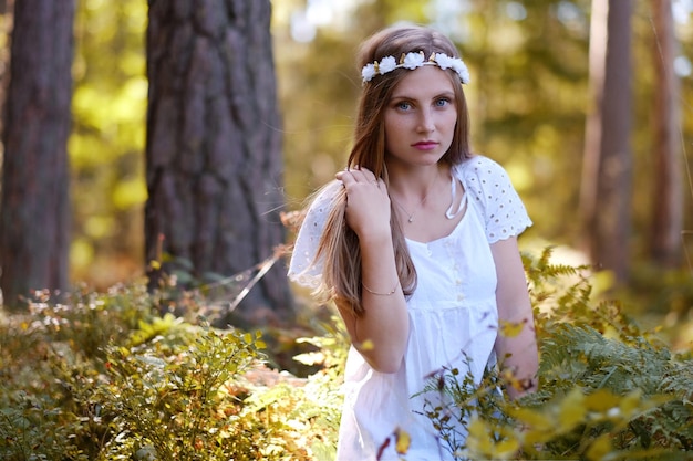 Mujer pecosa con círculo de flores en su retrato de cabeza en el bosque de otoño a la luz del día.