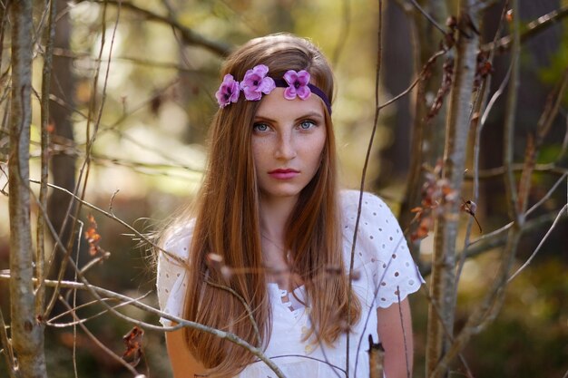 Mujer pecosa con círculo de flores en su retrato de cabeza en el bosque de otoño a la luz del día.