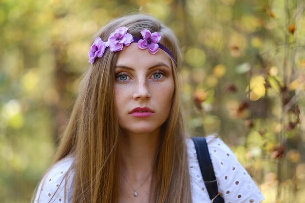 Mujer pecosa con círculo de flores en su retrato de cabeza en el bosque de otoño a la luz del día.