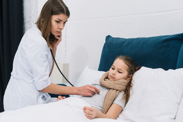 Mujer del pediatra que examina a la pequeña niña enferma con el estetoscopio