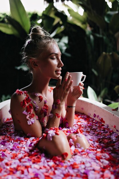 mujer con peinado de moda posando en el baño con taza de té. Encantadora dama europea disfrutando de spa en fin de semana y tomando café.