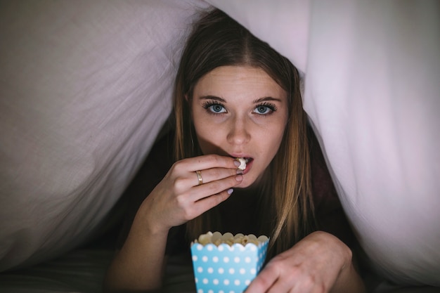 Foto gratuita mujer con película de observación de palomitas debajo de la manta