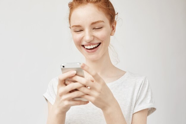 Mujer pelirroja alegre sonriendo mirando la pantalla del teléfono.