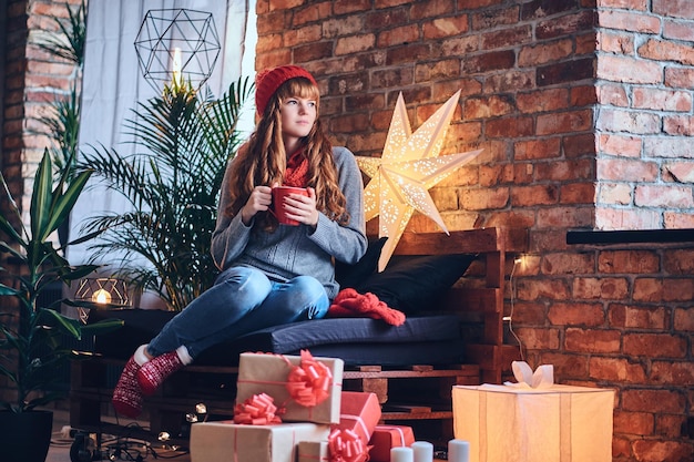 Mujer pelirroja bebe un café caliente en una sala de estar con interior de loft.