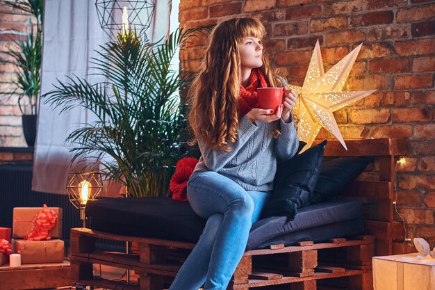 Mujer pelirroja bebe un café caliente en una sala de estar con interior de loft.