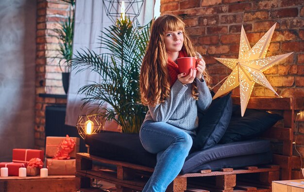 Mujer pelirroja bebe un café caliente en una sala de estar con interior de loft.