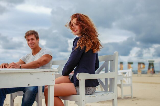 Mujer pelirroja y un chico sentado a la mesa en la playa.