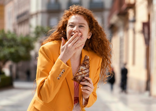 Mujer pelirroja comiendo algo de comida en la calle