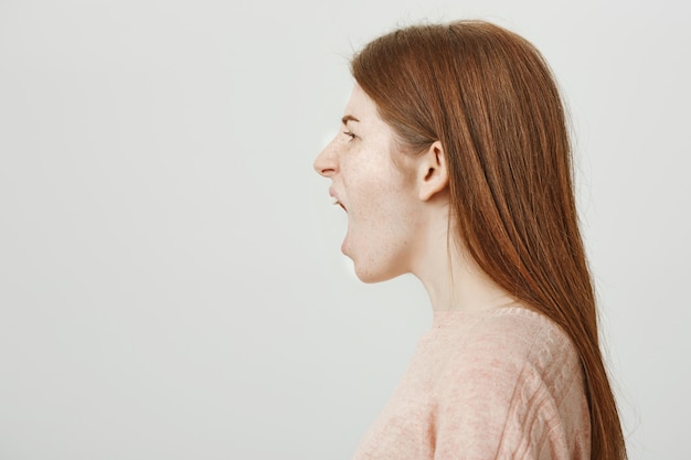 Mujer pelirroja enojada de pie perfil y gritando enojado