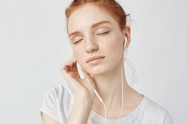 Mujer pelirroja escuchando música en auriculares con los ojos cerrados.