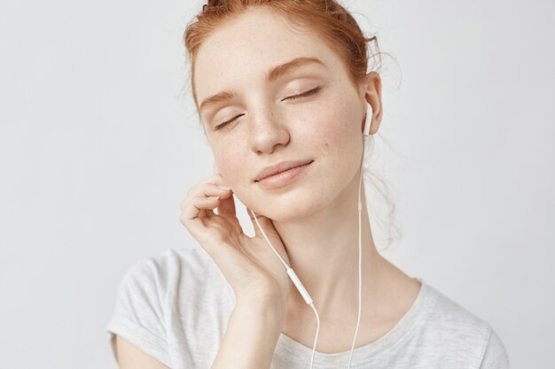 Mujer pelirroja escuchando música en auriculares con los ojos cerrados.