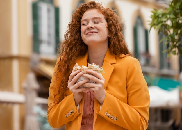 Mujer pelirroja feliz comiendo algo de comida en la calle