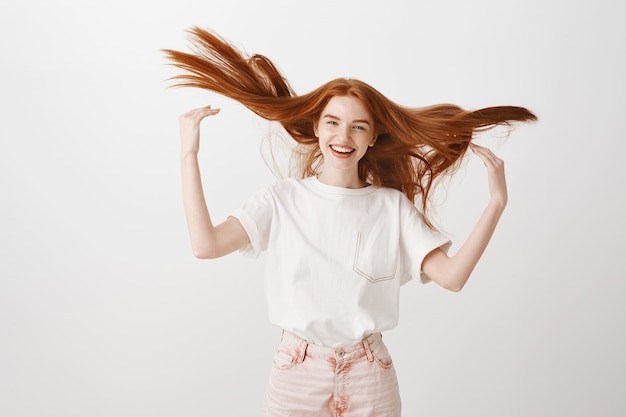 Mujer pelirroja feliz despreocupada tirando su cabello y sonriendo optimista