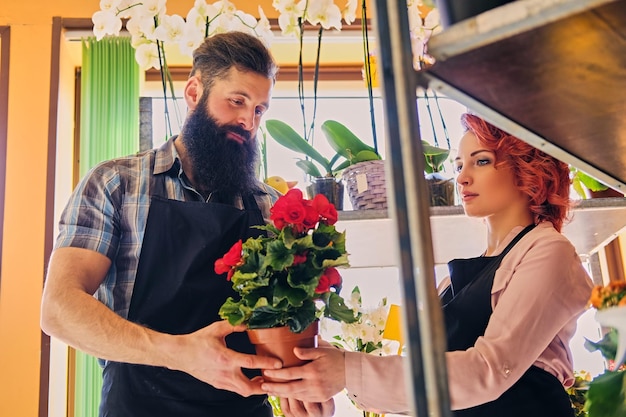 Mujer pelirroja y hombre tatuado barbudo vendiendo flores en una tienda de mercado.