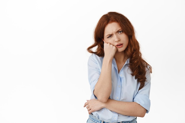 Mujer pelirroja molesta y aburrida mira con cara aburrida e irritada a la cámara de pie escéptica y sin diversión contra el fondo blanco Copiar espacio